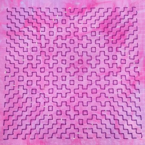 A piece of mottled dark pink/light pink fabric with a sashiko-style design embroidered on it with purple thread.  In the middle is the order 4 Fibonacci snowflake, surrounded by some small square motifs and zigzag lines. White thread has been used to take couching stitches over parts of the design where the purple stitches are twice as long as usual. The design has C4 symmetry, i.e. the only symmetries are from rotating it 90°, 180°, 270°, or 360°.