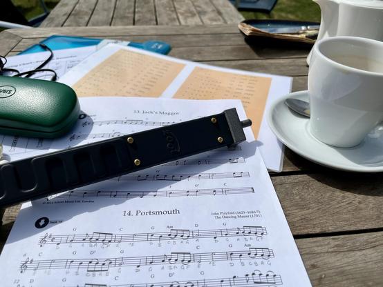 Photo of a weathered wooden café table cluttered with white teapot, cup and saucer, glasses case, reference charts, sheet music and Zoot (a long and slim boxy grey electronic musical instrument based on a baroque recorder). The tea and accompanying fruit scone weren't bad, if a little pricey.