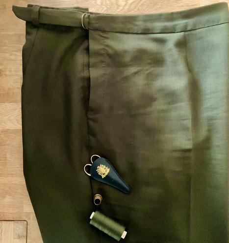 Oberer Teil einer Hose mit zweitilgem Bund (verstellbar) aus dunkelgrünem Stoff liegt auf einem Eichentisch.