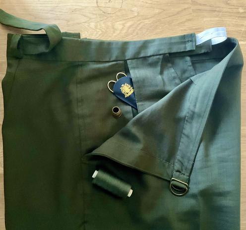 Oberer Teil einer Hose mit zweitilgem Bund (verstellbar) aus dunkelgrünem Stoff liegt auf einem Eichentisch