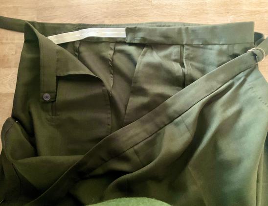Oberer Teil einer Hose mit zweitilgem Bund (verstellbar) aus dunkelgrünem Stoff liegt auf einem Eichentisch