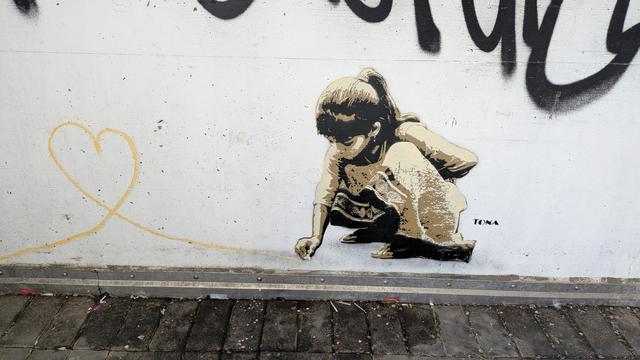 Street-Art auf einer weißen Wand im Stadion: Ein Mädchen malt mit Kreide ein Herz.