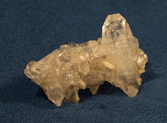 A crystal cluster of slightly brighter clarity but somewhat similar in "look" to Rock Quartz crystal is posed on deep blue velveteen. If you look closely, you can find tiny rainbows trapped in the crystals. This is Apophyllite, a relatively unknown crystal popularized in the New Age as a calming and meditation stone. Poona, India. Photo by Peachfront of my own specimen.