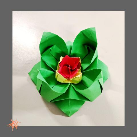 Foto einer Origamiblüte aus grünen, gelben und roten Papier.