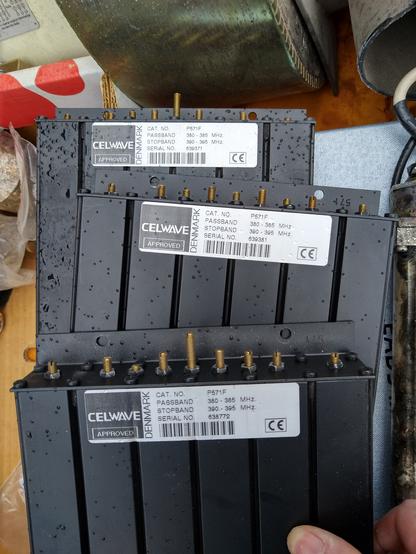 Picture of three black Celwave made six cavity flat pack filters for 380 - 385 MHz, with 390 - 395 MHz stop band.
Pictured with slight rain drizzle on them.