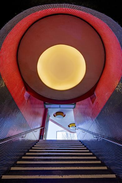 Look up wide angle view on huge round lamp with yellow light bulb on top of a black staircase leading to an exit at Fehrbellinerplatz metro station in Berlin.
