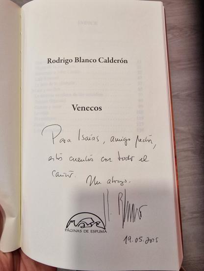 La imagen muestra la página de dedicatoria de un libro titulado "Venecos", escrito por Rodrigo Blanco Calderón. La página contiene una dedicatoria manuscrita a un "Isaías, amigo lector", deseándole que disfrute de los cuentos. La dedicatoria está firmada y fechada el 19 de mayo de 2025, con el logo de "Páginas de Espuma", la editorial.