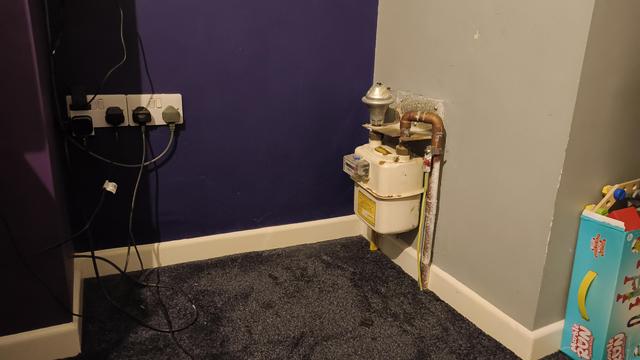 An awkwardly shaped old rusty gas supply about 2ft tall attached to a wall on the right hand side in the corner of an alcove.