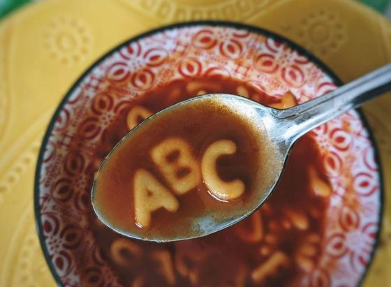 A spoonful of alphabet soup with the letters A, B, and C floating in the tomato broth.