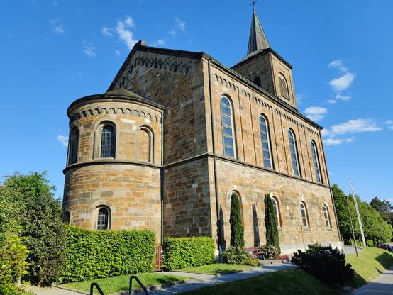 Eine alte Kirche vor blauem Himmel, umsäumt von Hecken und einzelnen kleinen Bäumen