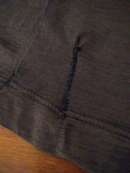 A black piece of fabric covers most of the photo, but there's a corner of wooden table to the bottom left. In the middle of the fabric there is a darned former rip with the textile bunching up at the top.