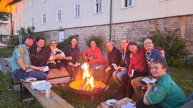 Die Erfurter Singerunde sitzt um eine Feuerschale mit Feuer auf Bierbänken.