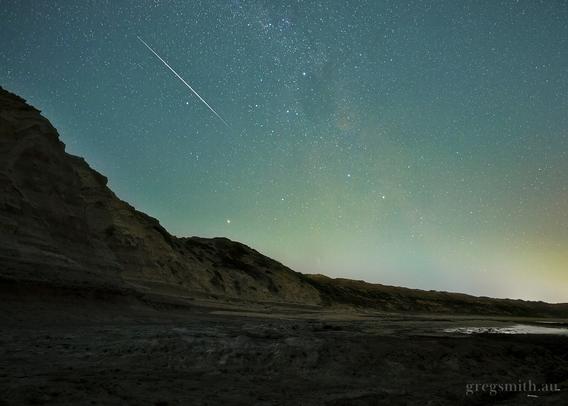A meteor streaking through the night sky, with a weathered cliff face in the foreground.