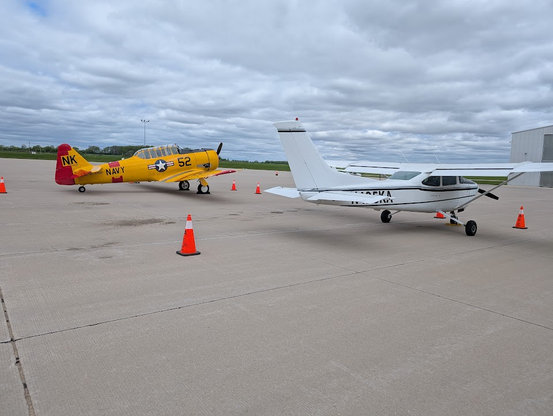 A North American T-6 Texan in yellow paint with NAVY painted in the side. There is a Cessna Skyhawk sitting next to it on the ground.