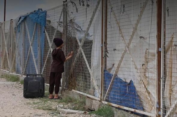 Un enfant derrière les grilles d’un camp.