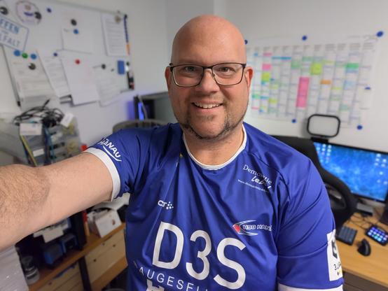 Daniel R. Schmidt steht am bundesweiteren Trikottag des Deutschen Olympischen Sportbundes im blauen Spieltrikot des Drittligisten HSG Hanau in seinem Büro und schießt ein Selfie.