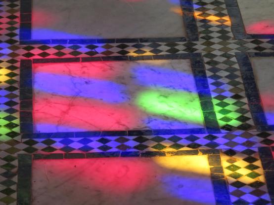 Sur un sol à carreaux noirs et blancs, les reflets rouge jaune bleu vert d'un vitrail