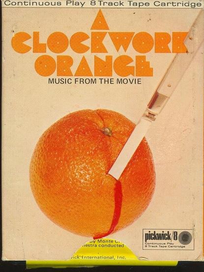 A photo of a vintage outer white and orange box to an 8-track cartridge tape entitled "A Clockwork Orange - Music From the Movie." Inset image shows a folding knife stuck into an unpeeled orange, with blood-like red liquid oozing down its side. Text at the top reads "Continuous Play 8 Track Tape Cartridge." The Pickwick 8 Label is at the bottom right corner.