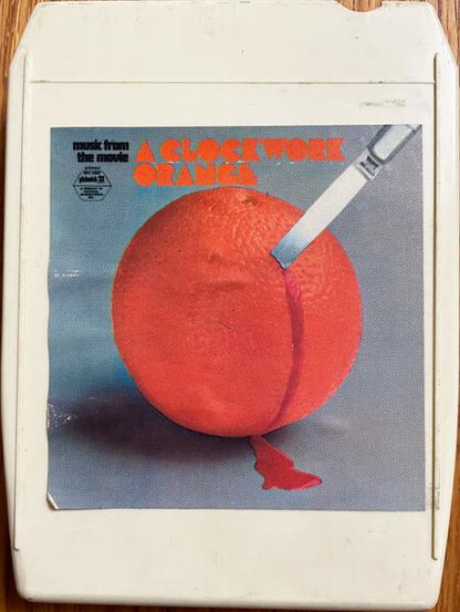 A photo of a vintage white plastic 8-track cartridge tape entitled "A Clockwork Orange - Music From the Movie" inset with same knife & bleeding orange image described previously.