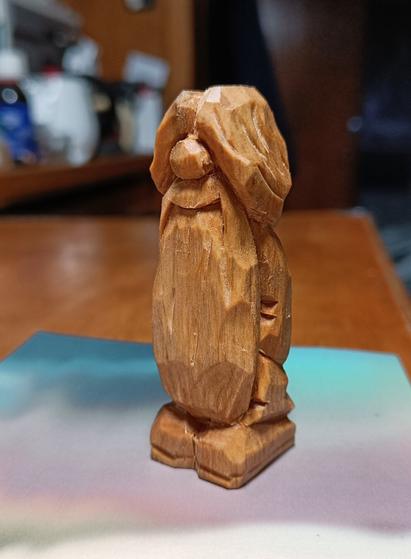 Wood carving of a little bearded hippie character that has long hair tied back in a pony tail.