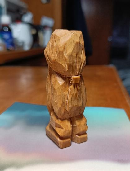 Wood carving of a little bearded hippie character that has long hair tied back in a pony tail.