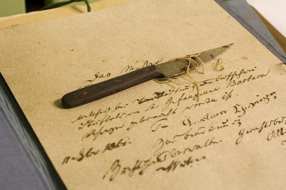 Ein kleines spitzes Messer mit Holzgriff mit einem Faden an der Klinge liegt auf einem alten Schriftstück.