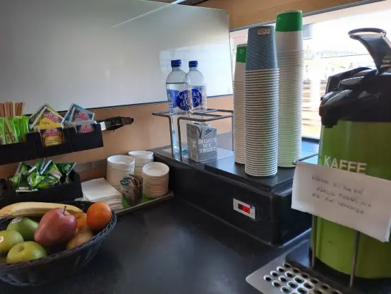 Photograph (colour): A table with take away muggs, water bottles, fruit and a thermos with a note in Swedish saying "Hope you will have a great Tuesday and a nice week".