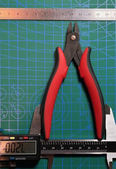 Top-down photograph of a pair of Hakko CHP-170 flush cutters.  The handles are compressed between the jaws of a caliper.  The caliper's digital readout says 72.00.  Above the cutters is a steel ruler.  The tip of the cutters is almost centered on the ruler's 100 millimeter point.  All these things are sitting, aligned, on a cutting mat marked in centimeter squares.