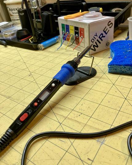 Photo of an incredibly old and janky soldering iron on a yellow cutting mat with various electronic components in the background.
