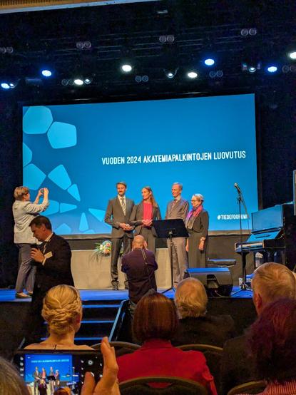Olle Järv received his award, as did Emilia Nordlund for her work in the field of food science. They are on the stage with the directors of the Research Council of Finland.
