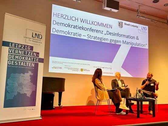 Foto vom Panel "Gefährdete Demokratie? Perspektiven auf Desinformation" auf der Demokratiekonferenz. Es diskutieren gemeinsam Prof. Dr. Christian Hoffmann (Universität Leipzig) und Holger Marcks (Machine Against The Rage, IDZ Jena) moderiert von Sofija Pavlenko.