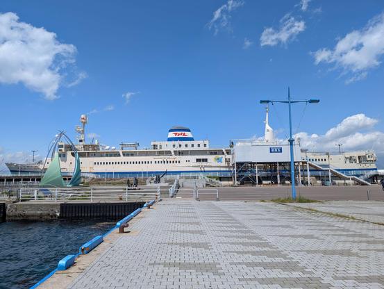 A photo of a large multi-deck ocean ferry moored permanently in port. A bright blue sky is overhead.