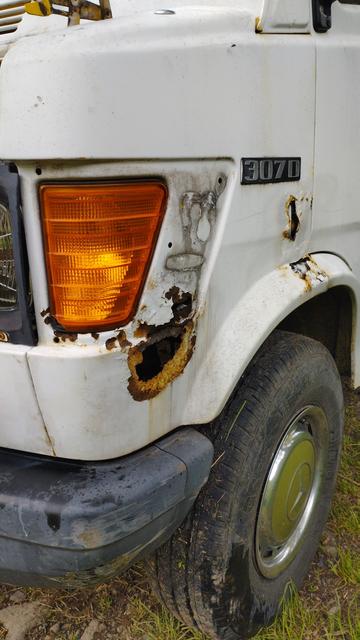 L'aile gauche du tawamusi sans l'enjoliveur de clignotant gauche. Il y a des traces de rouille et un trou de 10 cm. La carrosserie est censée être blanche. Il y a aussi le coin du pare-choc, la roue, son enjoliveur et le logo 307d