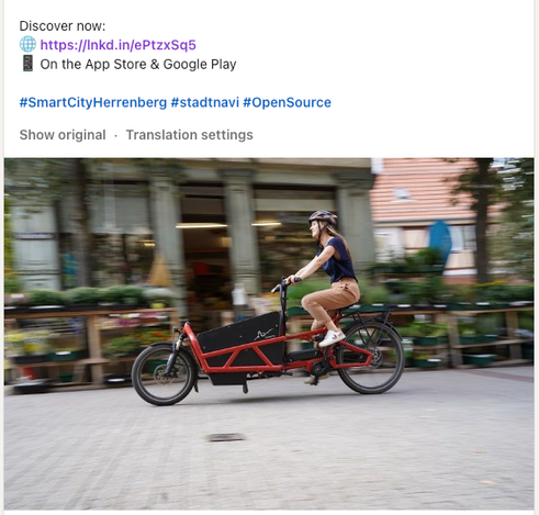 A promotional social media post featuring a woman riding a modern cargo bicycle through an urban street, with the caption encouraging viewers to "Discover now" and linking to an app available on the App Store and Google Play.