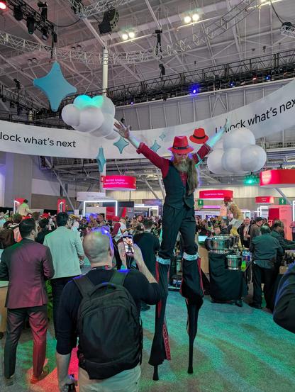 A performer on stilts wearing a red fedora at RH summit expo hall