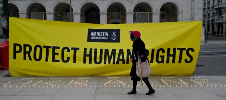 woman walks by a banner and candles in Praça do Comercio set up by Amnesty International to protest human rights violations on the 2nd anniversary of Russia's invasion of Ukraine