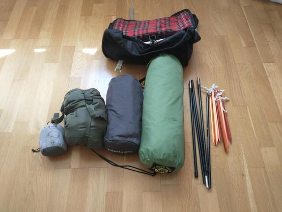 Carradice-Satteltasche ausgepackt und von links Pakete mit: kleines Kopfkissen, Schlafsack, Isomatte, Zeit, Zeitstangen, Zeltheringe