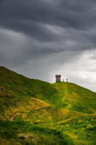 Landschaftsfotografie im Hochformat; ein Fussweg führt über eine Wiese zu einem kleinen Häuschen.