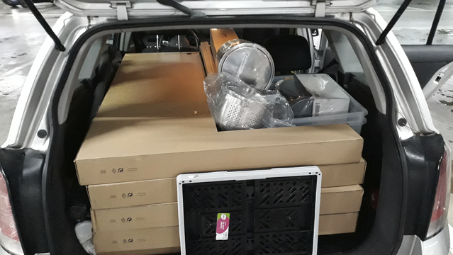 The back of a hatchback car with the door open, and stacked almost to the top with L-shaped boxes and many other items tucked behind them. A folder plastic crate is set up against the boxes, using up the last few centimetres of space.