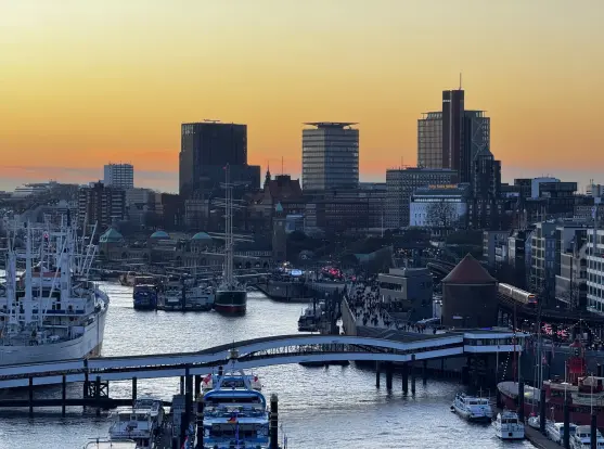 The sunset behind some tall modern buildings and some , as well as the Landungsbrücken in the foreground.