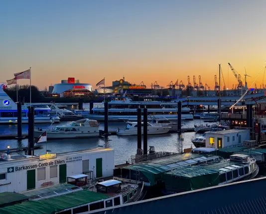 The sunset behind some harbour cranes, as well as multiple boats in the foreground.