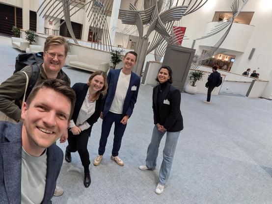 Selfie im Europäischen Parlament. Erik Tuchtfeld fotografiert sich mit Ulrich Berger (mit Rucksack), Anke Obendiek, Bendix Sältz und Marlene Straub. Die Gruppe steht verteilt vor einer Metallskulptur. Alle lächeln in die Kamera.