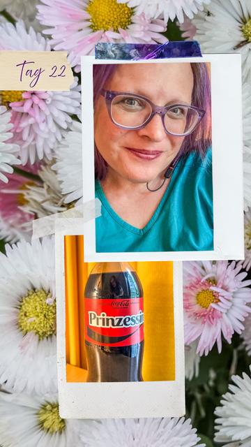 Zwei Polaroid-Rahmen liegen übereinander auf einem Hintergrund aus zarten rosa-weißen Margeritenblüten. Im oberen Polaroid ist ein Selfie von Vera zu sehen: Sie lächelt sanft, trägt ein türkisfarbenes Oberteil, lila Brille und dezentes Make-up mit dunklem Lippenstift. Ihre Haare schimmern violett, ein schwarzer Kopfhörer liegt locker um ihren Hals. Im unteren Polaroid steht eine Coca-Cola Zero Flasche mit einem personalisierten Etikett, auf dem „Prinzessin“ steht, vor einem leuchtend gelben Hintergrund. Oben links auf dem Bild steht handschriftlich „Tag 22“.