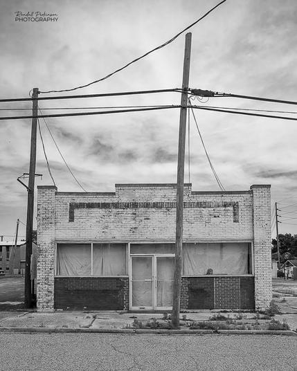 An old abandoned commercial building with overhead power and communication wires.  A female mannequin head with a wig sits in a window.  Very creepy.