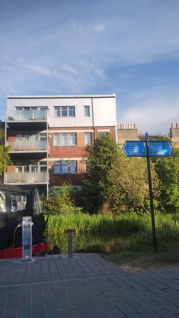 Four storey brick and metal building, commercial architecture by the Union Canal, now refashioned into waterside apartments, catching evening light, with a sign pointing to destinations & distances along the canal in the foreground