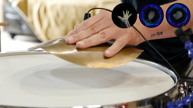 A hand holding a cymbal microphone hybrid over a drum head.
