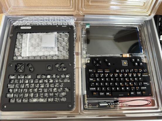 Parts of a uConsole in a there box, on the left is a black metal front shell, on the top right is the bare screen and bellow it is the keyboard module.