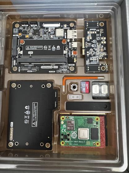 Internal components of the uConsole laid out in the box, there are 3 black circuit boards, an orange Allen key, a 32gb micro and card card and a raspberry pi cm4 compute module.