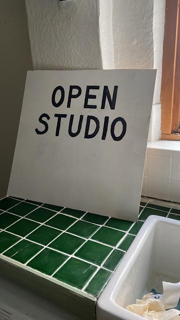 Black and white sign saying OPEN STUDIO propped against a kitchen wall on green-tiled surface.