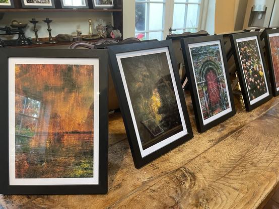 Photographs displayed on an oak table in black frames. Too distant to make out detail but provide a sense of their colour palette. In background others propped up on a book shelf!